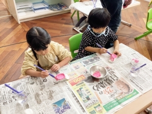 桃色の絵の具で雛人形の体に色を塗る生徒たち