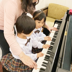 グランドピアノでお友だちと先生と3人で連弾する生徒たち