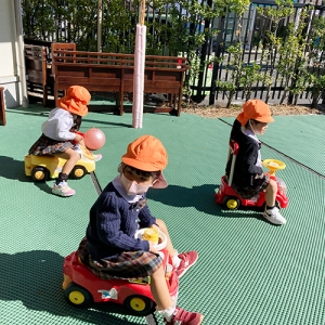 園庭で車に乗って遊ぶ生徒たち