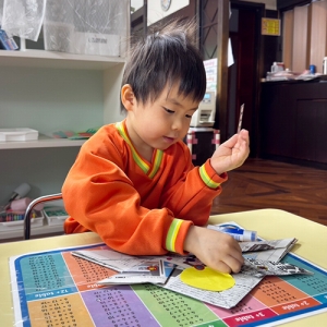 新聞紙のかぶとに折り紙の飾りをのりで貼る生徒