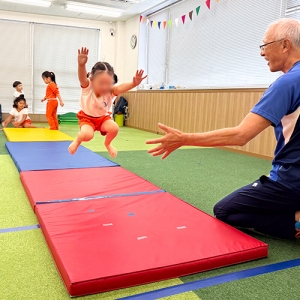 マットでジャンプする生徒と見守る先生