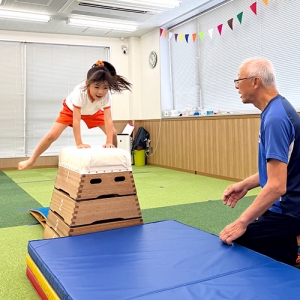 跳び箱を跳ぶ生徒と見守る先生