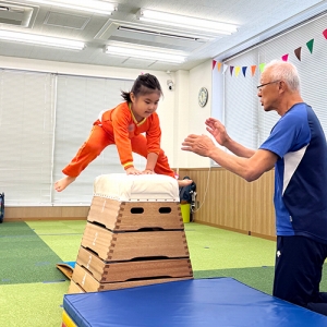 跳び箱を跳ぶ生徒と見守る先生