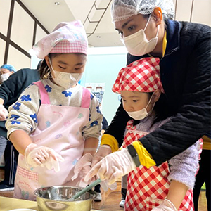 先生と協力してボールの中の材料を混ぜる生徒たち