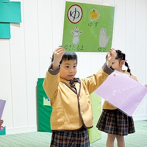 大きな画用紙を頭上に掲げてひらがなの発表をする生徒