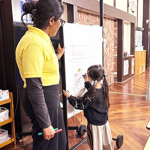 ホワイトボードに書く生徒と見守る先生