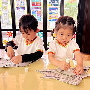 新聞紙かぶとにのりを塗る子どもたち