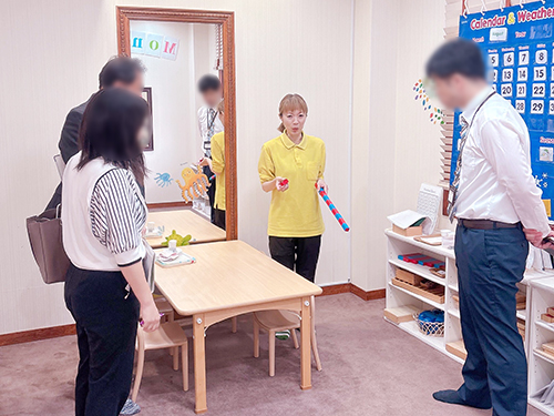 ママーズキッズアカデミーへ視察に訪れた羽島市教育委員会学校教育課のみなさんに話をする英語講師