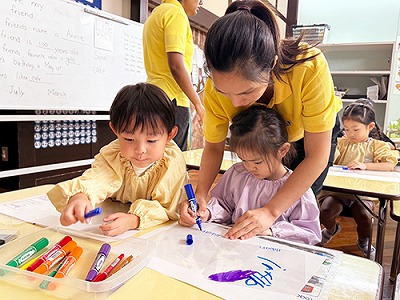 風車に色を塗る子どもを指導する先生