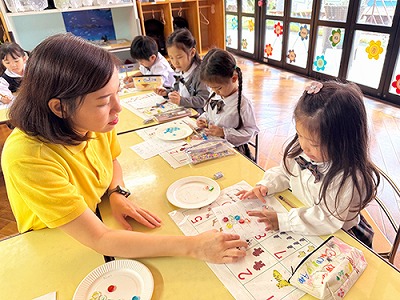 おはじきで数をかぞえる生徒たちを指導する先生